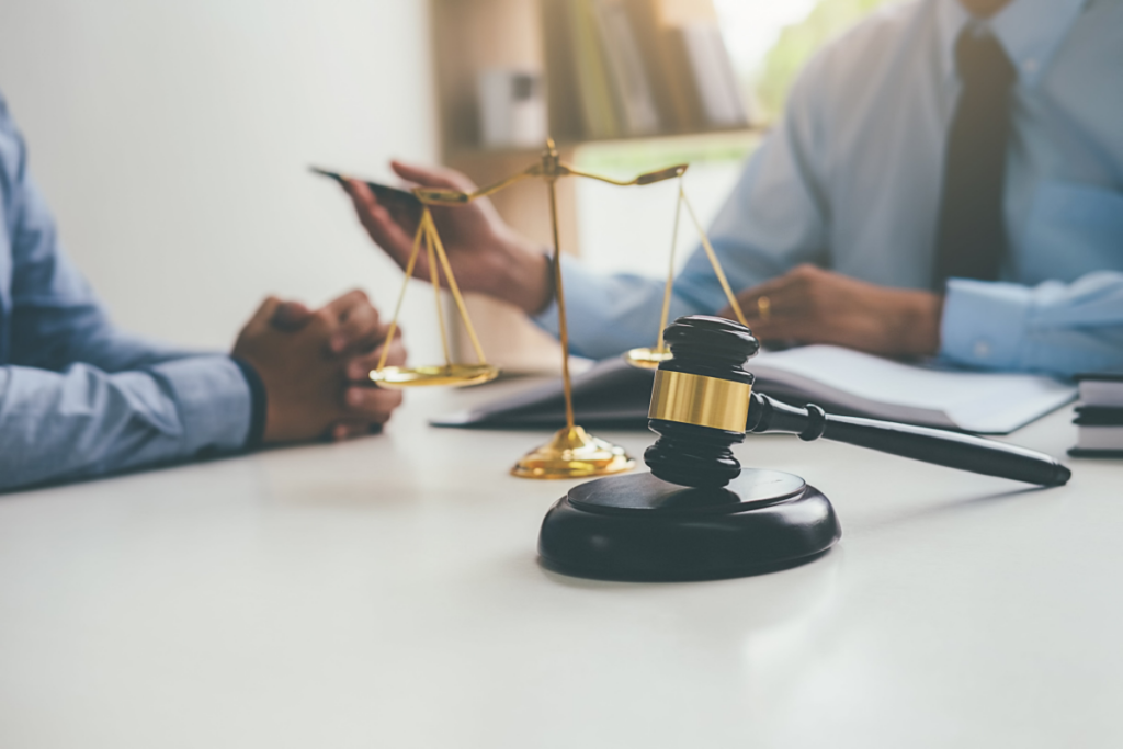 A lawyer and judge sitting at a table with scales of justice in a courtroom.